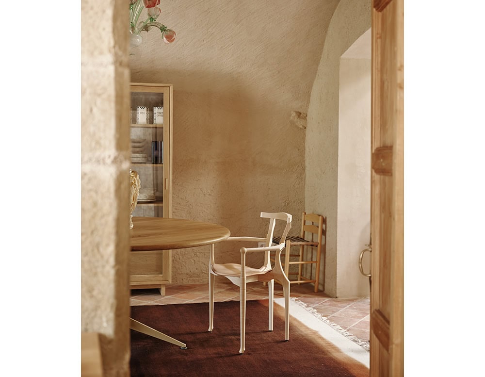 A cream-colored BD Gaulino Chair pairs with a round wood table in a softly textured interior. The chair's delicate silhouette complements the warm, rustic atmosphere.