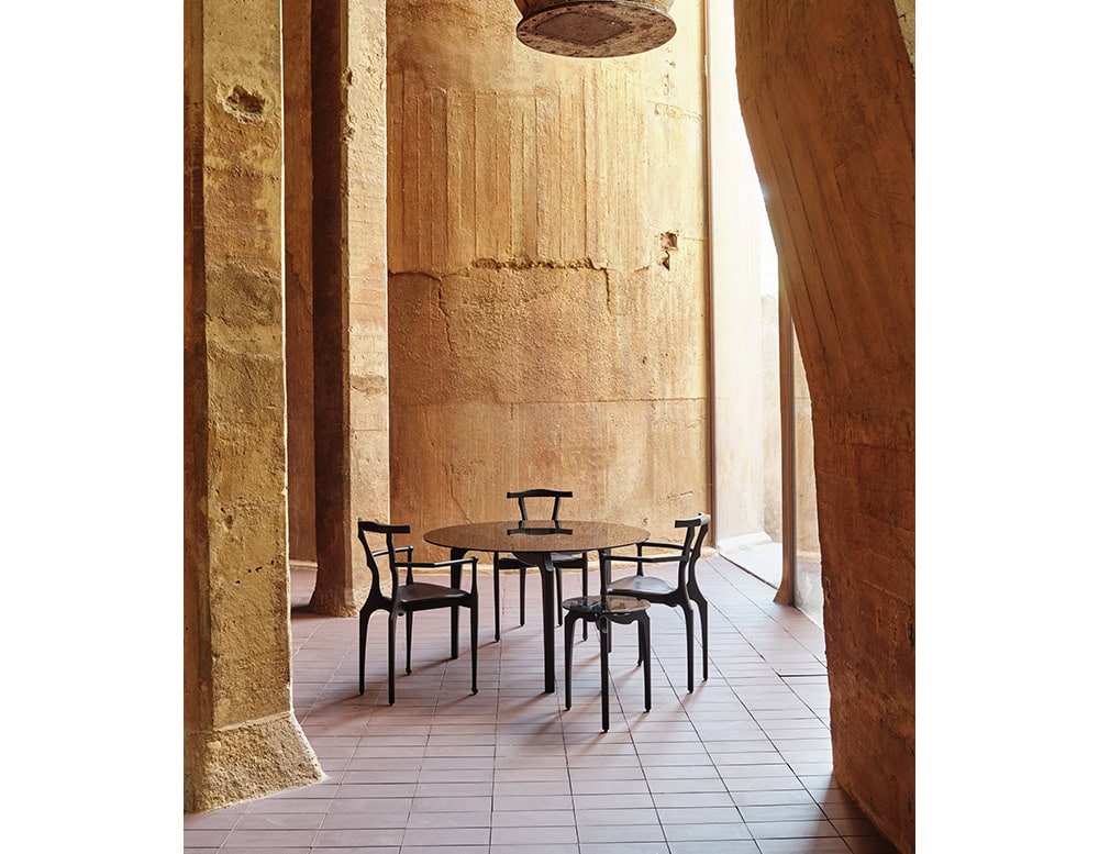 A group of black BD Gaulino Chairs surrounds a matching round table. The sculptural design contrasts with the textured stone architecture, creating an elegant and inviting setting.