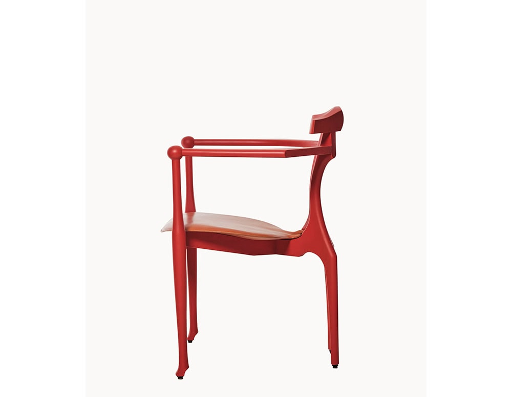 Elegant red frame with softly rounded armrests and sculpted legs, paired with a contoured tan leather seat. The side profile highlights the chair’s fluid craftsmanship and balanced proportions.