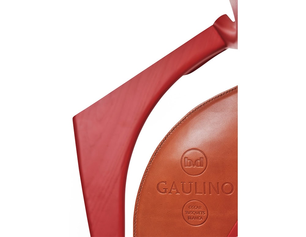 Close-up of the Gaulino Easy Chair, showcasing its sculptural red wooden frame and embossed leather seat. The craftsmanship highlights elegant curves and rich materials designed by Oscar Tusquets Blanca.
