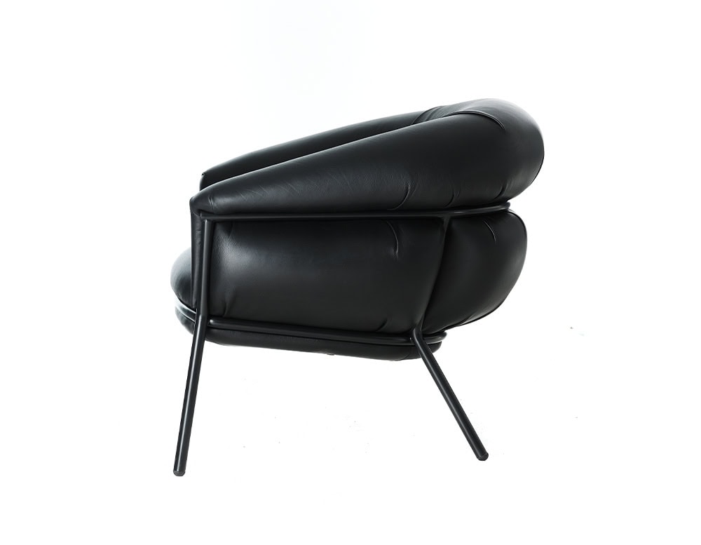 Side angle of the BD Grasso Armchair in black leather highlights its exaggerated padded form spilling over a sleek black steel frame. The soft, voluminous upholstery contrasts with the minimal structure, showcasing its relaxed and bold character.