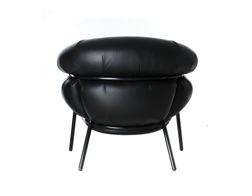 The BD Grasso Armchair is shown from the back, fully upholstered in black leather with its signature overstuffed cushions. The rounded volumes extend beyond the black metal frame, emphasizing its playful yet robust design.