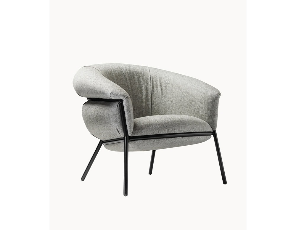 The BD Grasso Armchair is shown in a light grey textile with a black lacquered metal structure. Its soft upholstery intentionally overflows the frame, emphasizing comfort and casual elegance.