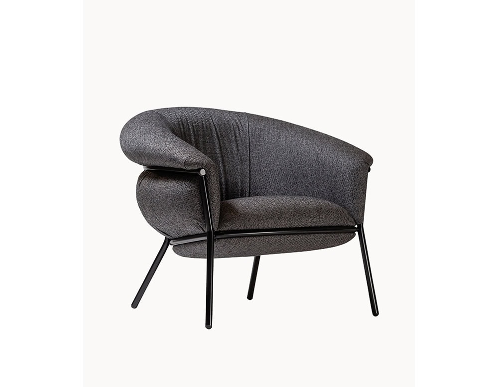 The BD Grasso Armchair appears in a textured dark grey fabric with a black lacquered metal frame. Its oversized cushions extend beyond the structure, creating a relaxed and inviting silhouette.