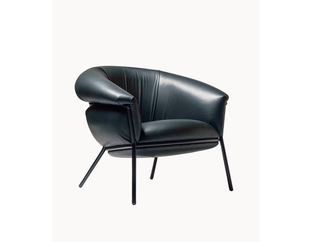 The BD Grasso Armchair appears in a black leather version with matching black metal legs. The voluminous upholstery spills generously over the frame, emphasizing its soft and inviting form.
