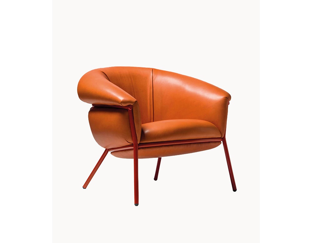 The BD Grasso Armchair is shown in its full form, upholstered in rich cognac leather with a red-lacquered metal base. Its bold seat appears to overflow from the frame, creating a relaxed and unconventional silhouette.