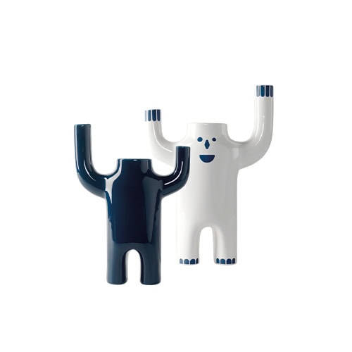 A pair of Happy Susto Vases is shown with expressive forms. The glossy dark blue vase contrasts with the white one, which features hand-painted eyes, a nose, and a smile, both raising their arms in a joyful, sculptural gesture.