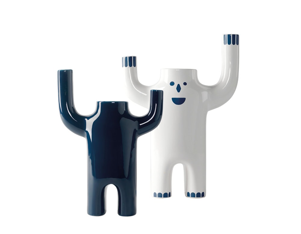 Playful, anthropomorphic forms. One in glossy deep blue, the other in white with cheerful face details, both with raised arms creating a whimsical and sculptural silhouette.