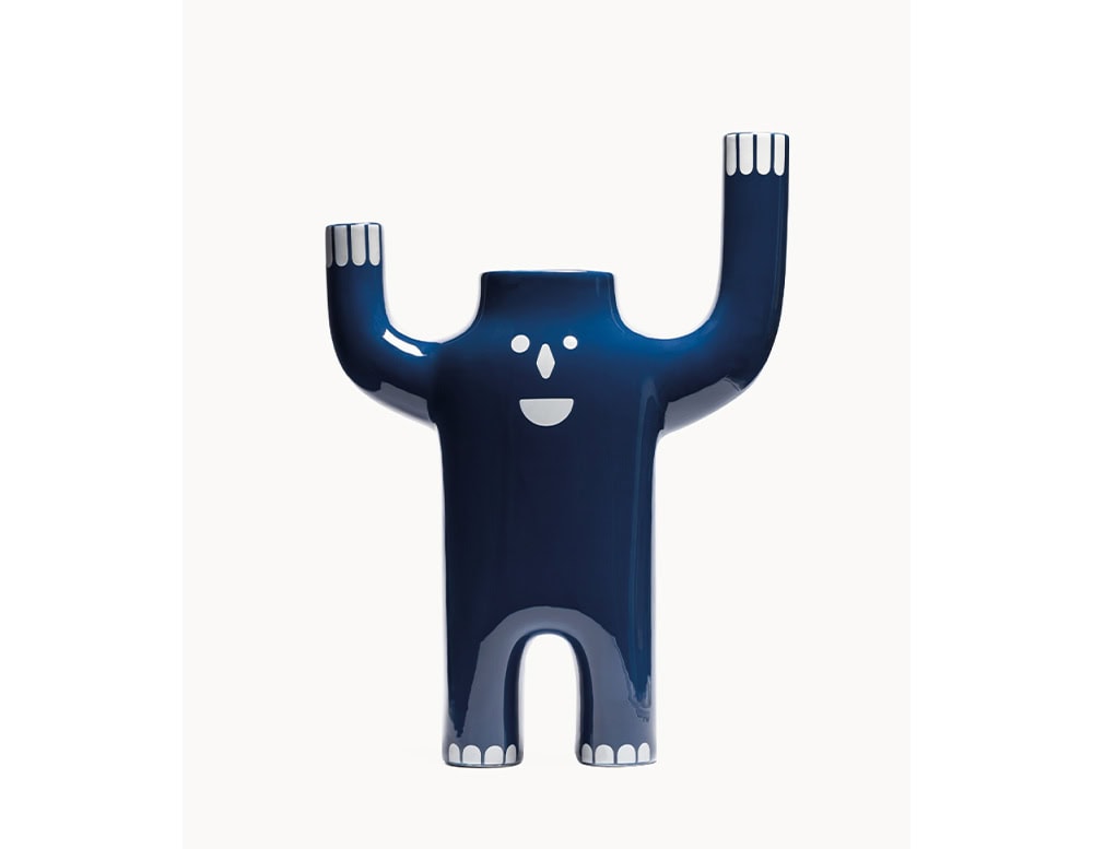 Glossy blue ceramic vase shaped like a joyful figure with arms raised, detailed with white facial features and fingertips. Its bold form and playful design make it a standout decorative accent.