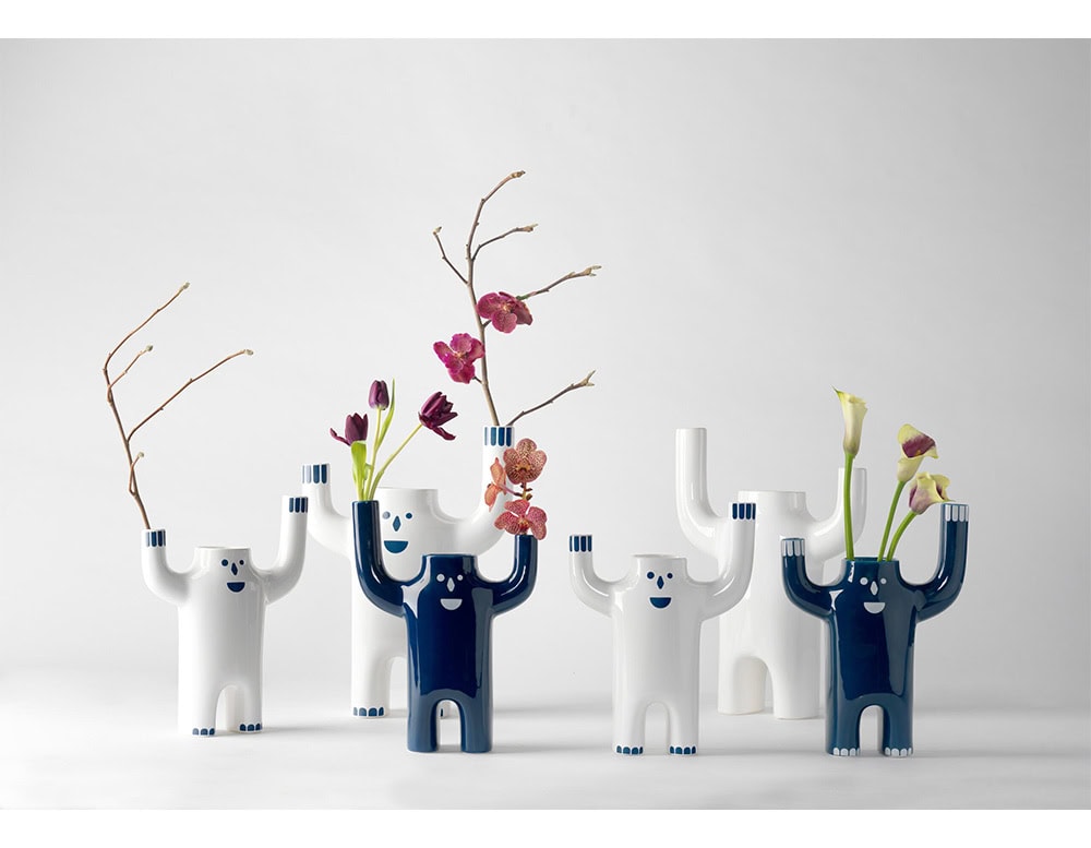 Glossy ceramic vases shaped like cheerful figures with raised arms, finished in deep blue and bright white. Their playful faces and upright stance add personality and charm to floral arrangements.
