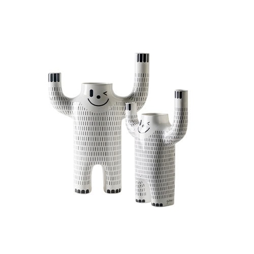 Two smiling ceramic figures with arms raised in a joyful pose, decorated with vertical black lines and playful facial expressions. Their quirky form and glossy finish create a fun, sculptural pair.