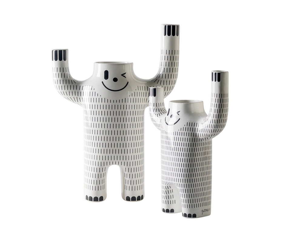 Two white ceramic figures with raised arms, each featuring a winking smile and vertical dash patterns. Their playful shapes and varying sizes create a joyful, character-like duo.