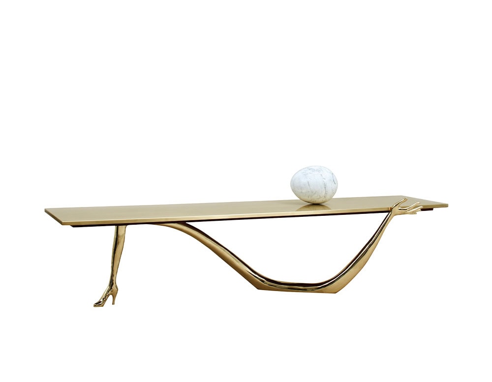 A sculptural coffee table with a golden top, supported by a bronze leg and arm. A marble sphere rests on the surface, blending surreal details with elegant design.