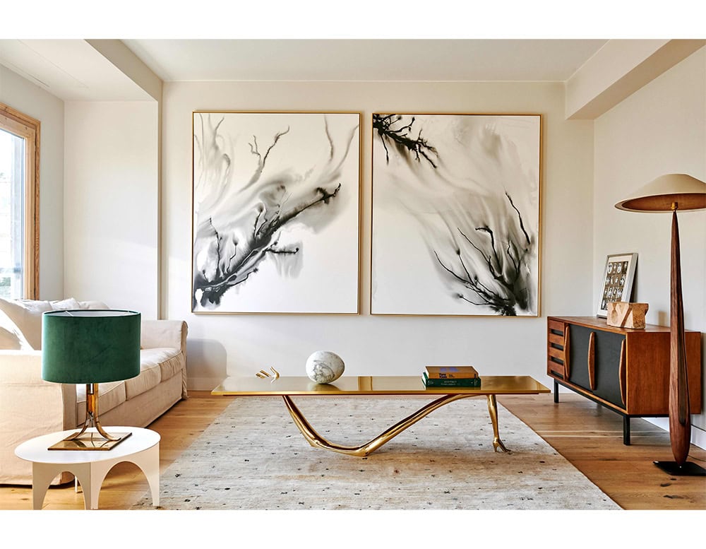 Leda Coffee Table with sculptural bronze legs and polished top. Paired with green velvet lamp, marble sphere, abstract art, and wood credenza, it creates a warm, modernist living space.