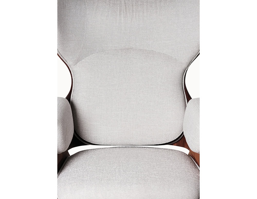 Lounger Armchair with a smooth walnut shell and off-white upholstery. The close-up view highlights its precise stitching, supportive curves, and plush arm cushions that offer refined comfort.