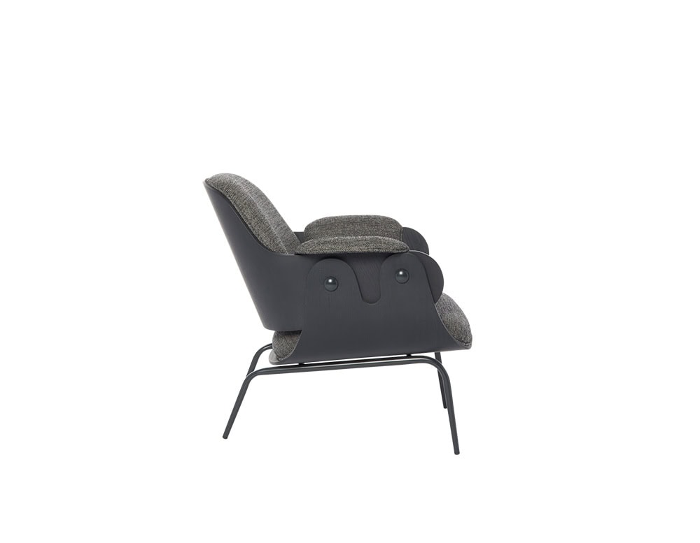 Low Lounger Armchair shown in side view with textured grey fabric and dark sculpted wood arms. Set on minimalist black metal legs, its soft profile and ergonomic shape provide relaxed comfort with strong visual character.