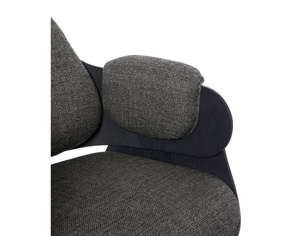 Low Lounger Armchair in dark woven fabric. The textured upholstery contrasts with the matte black wood frame and curved cushion detail, creating a tactile and refined design focused on comfort and craftsmanship.