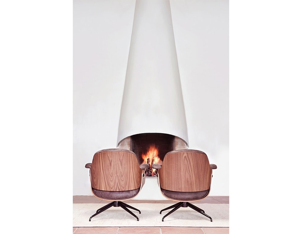 Pair of Low Lounger Armchairs with walnut backs and dark suede upholstery. Positioned symmetrically by a sculptural fireplace, enhancing the cozy ambiance with mirrored elegance and soft lighting on terracotta flooring.