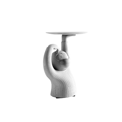 The BD Monkey Side Table appears in a full view, featuring its curved silhouette and playful posture. The table's surface is supported by the monkey's upraised arm, combining sculpture and function in a single concrete form.