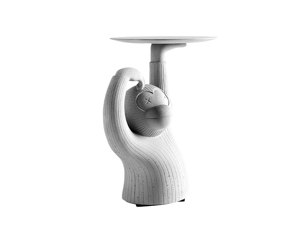 The BD Monkey Side Table is shown from a frontal angle, capturing the figure's closed eyes and serene expression. Its concrete finish with textured lines gives the piece a playful yet architectural presence.