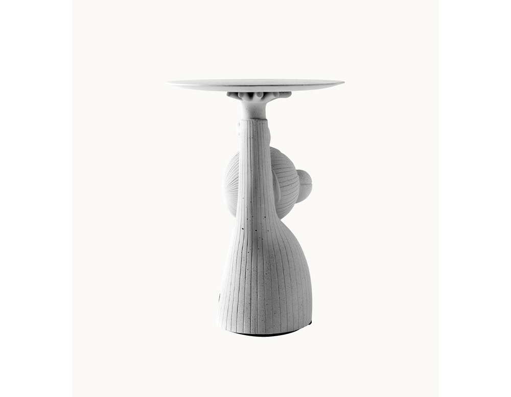 A sculptural monkey figure holds a tray aloft, crafted entirely in concrete. Vertical grooves and a speckled texture accentuate the playful yet architectural silhouette.