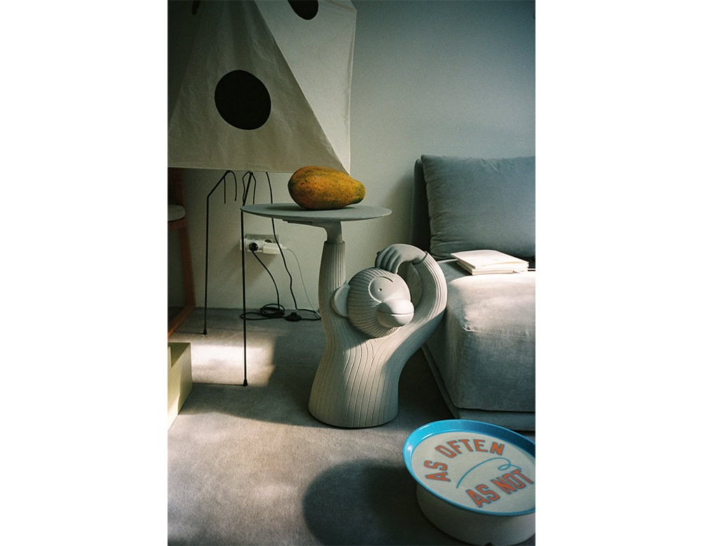 A playful side table shaped like a monkey holding up a tray. Its bold, sculptural design adds character to the room, styled next to a grey sofa with books and a fruit accent on top.