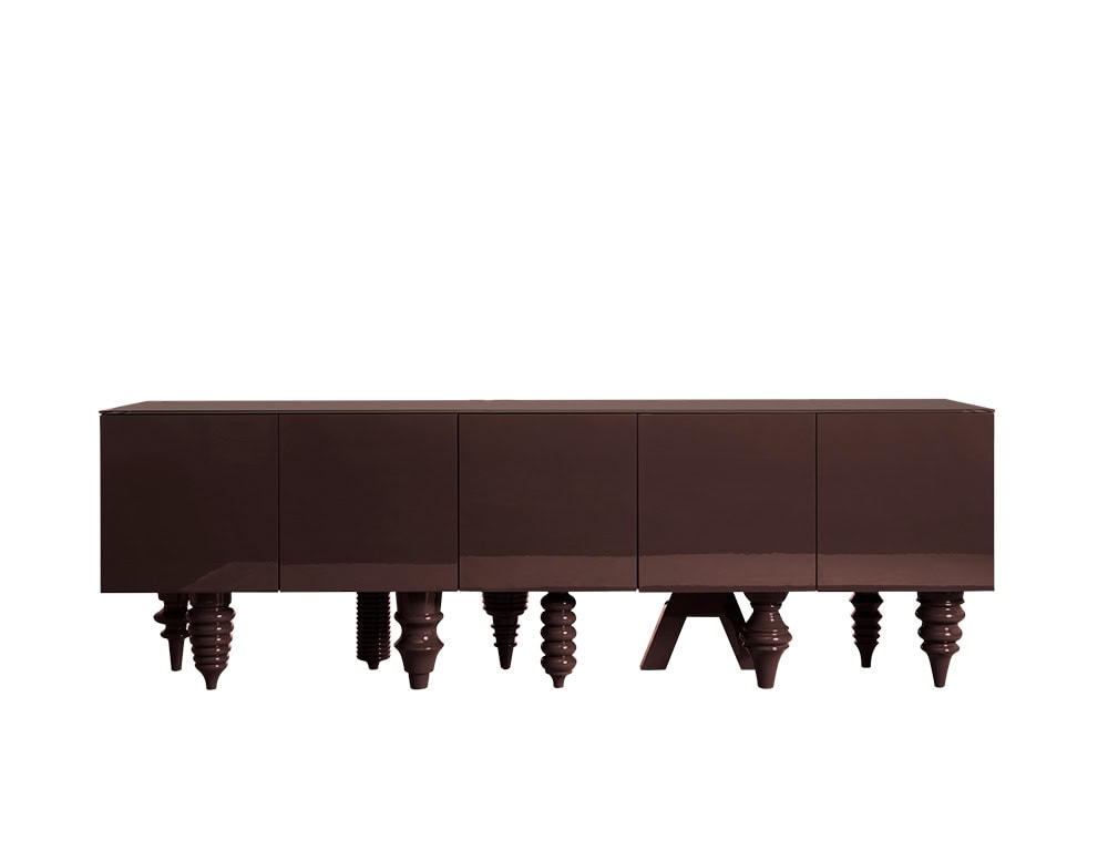 A rich brown cabinet finished in a reflective polished surface. The structure is clean and minimal, while the base plays with a mix of legs in varied shapes and proportions. Each element creates contrast between simplicity and decorative detail.