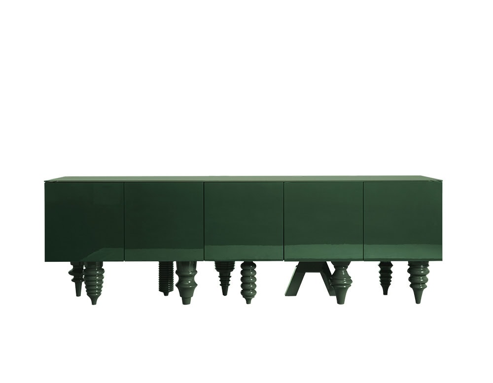 A deep green cabinet with a sleek glossy finish and a bold mix of ornamental legs, each one different, from spiraled to angular, creating a playful contrast beneath a minimalist geometric surface.