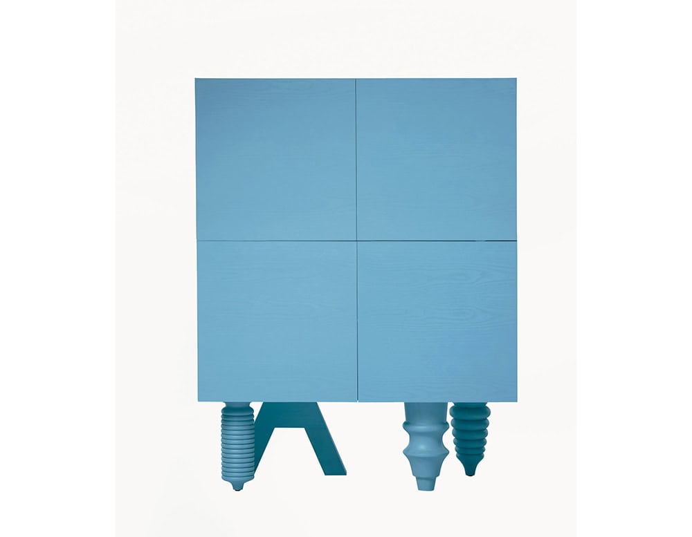 A bold blue cabinet with a minimalist grid front and an eclectic mix of sculptural legs—ribbed, angular, and rounded forms come together in a playful, architectural composition.