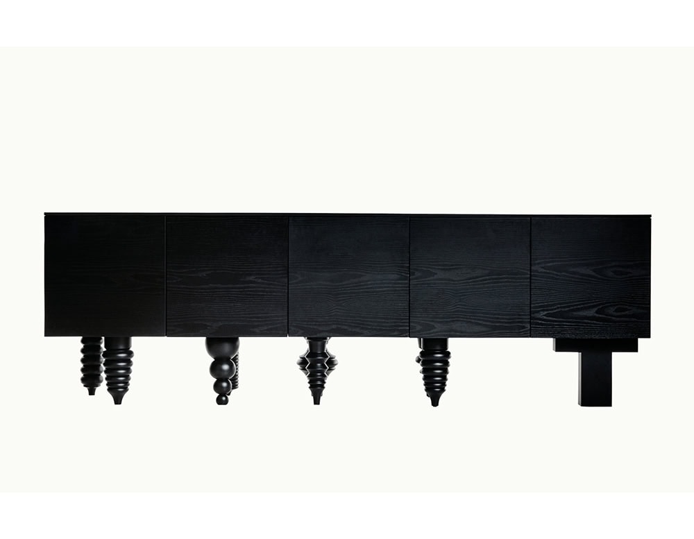 Sleek black wood cabinet with a smooth front and a striking mix of sculptural and block legs, blending bold geometry with refined craftsmanship.