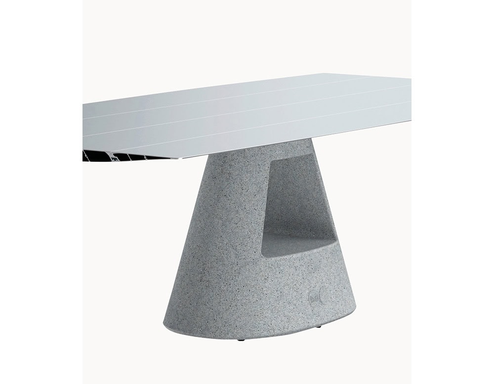This close-up shows the BD Table B's smooth aluminum surface resting on a textured grey concrete base. The geometric cutout in the base adds structural character and visual interest.