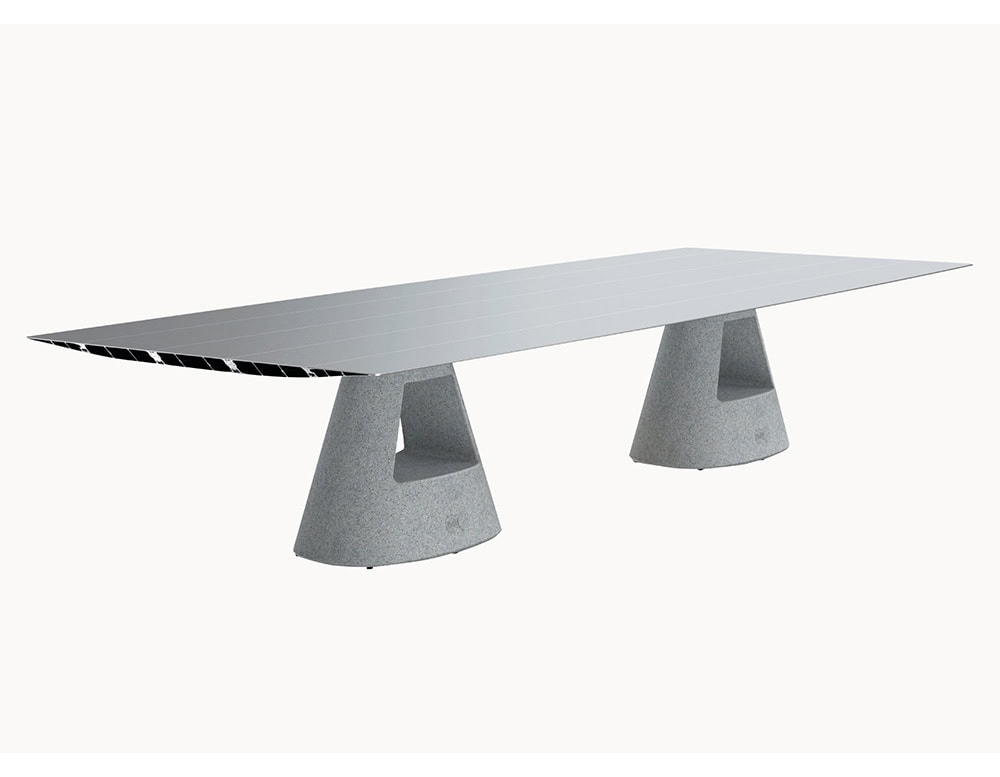 The BD Table B showcases a long, aluminum tabletop paired with two sturdy concrete bases. The materials combine light metallic surfaces with robust grey stone, creating an industrial yet elegant aesthetic.
