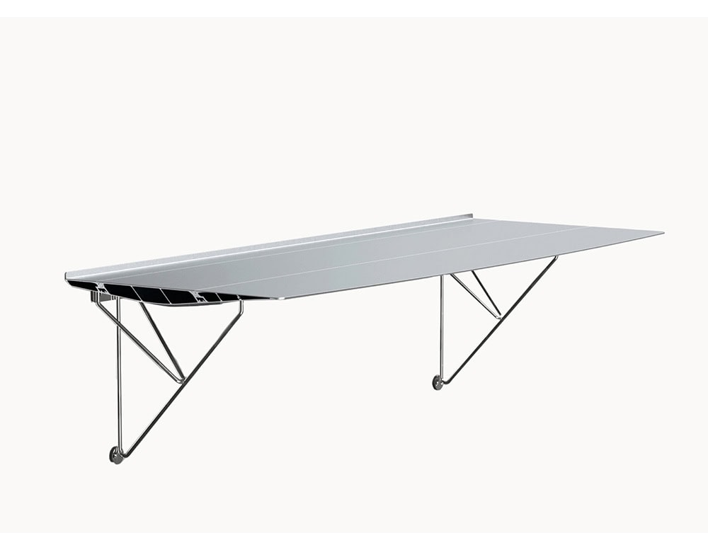 The BD Table B is displayed with a wall-mounted leg configuration, emphasizing its cantilevered design. The aluminum tabletop is paired with minimalist stainless steel supports that attach directly to the wall, creating a floating visual effect.