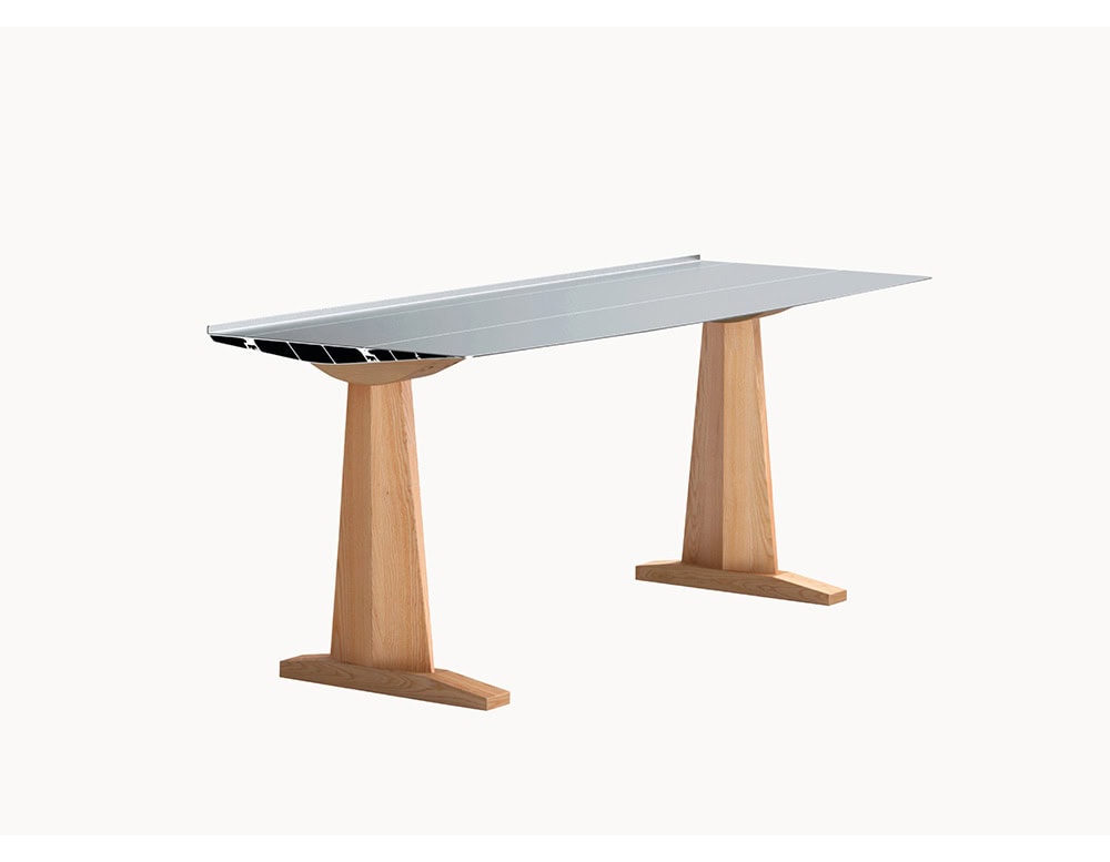 The BD Table B features a slim aluminum tabletop with a brushed finish, paired with solid oak trestle-style legs. The combination highlights structural elegance and a subtle mix of industrial and natural materials.