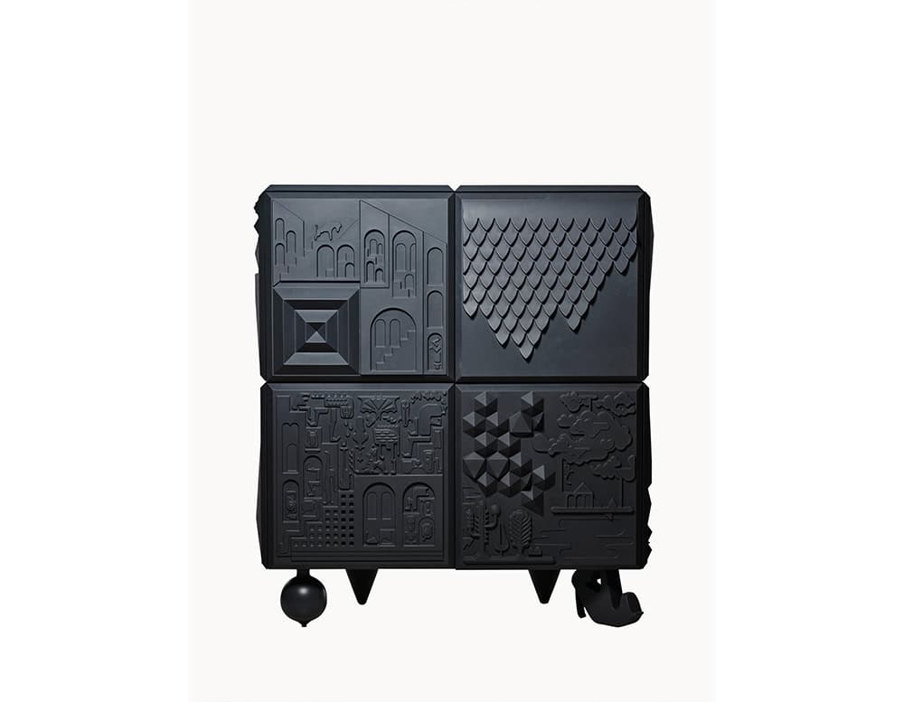 Matte black cabinet composed of four graphic panels, each with unique sculptural reliefs evoking urban, architectural, and geometric motifs. It rests on varied sculptural legs, including a sphere, a cone, and a stylized high heel.