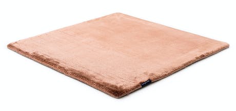 rug made of shiny velvet fabric in a salmon color tone a white background