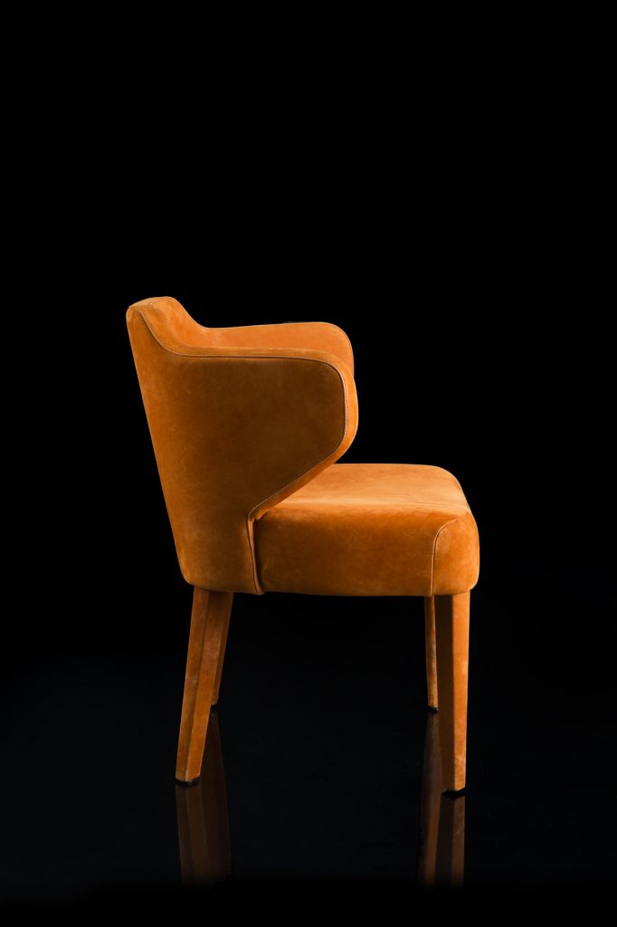 EX Tra Chair upholstered in orange leather and four wood legs on a black background.