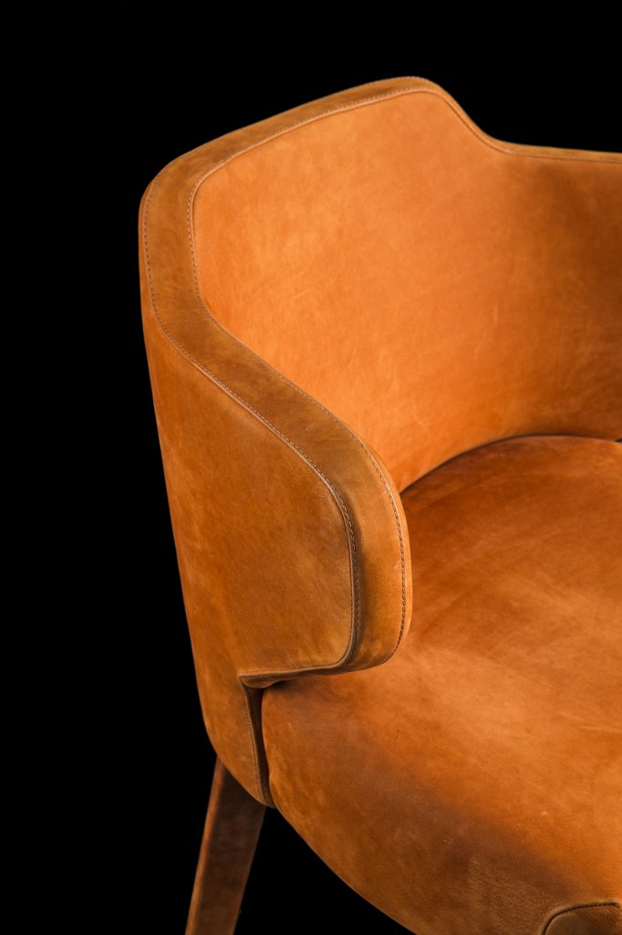 Closeup of EX Tra Chair upholstered in orange leather and four wood legs on a black background.