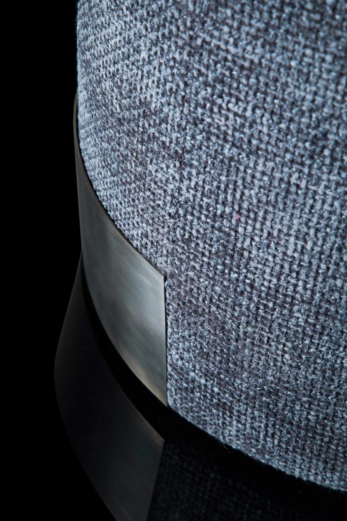 Closeup of Gelly Pouf upholstered in gray leather and a base in black steel on a black background.