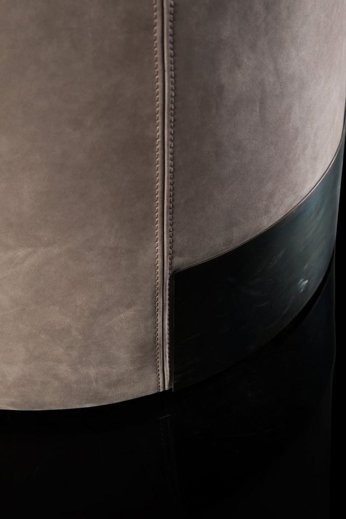 Closeup of Gelly Pouf upholstered in pink leather and a base in black steel on a black background.