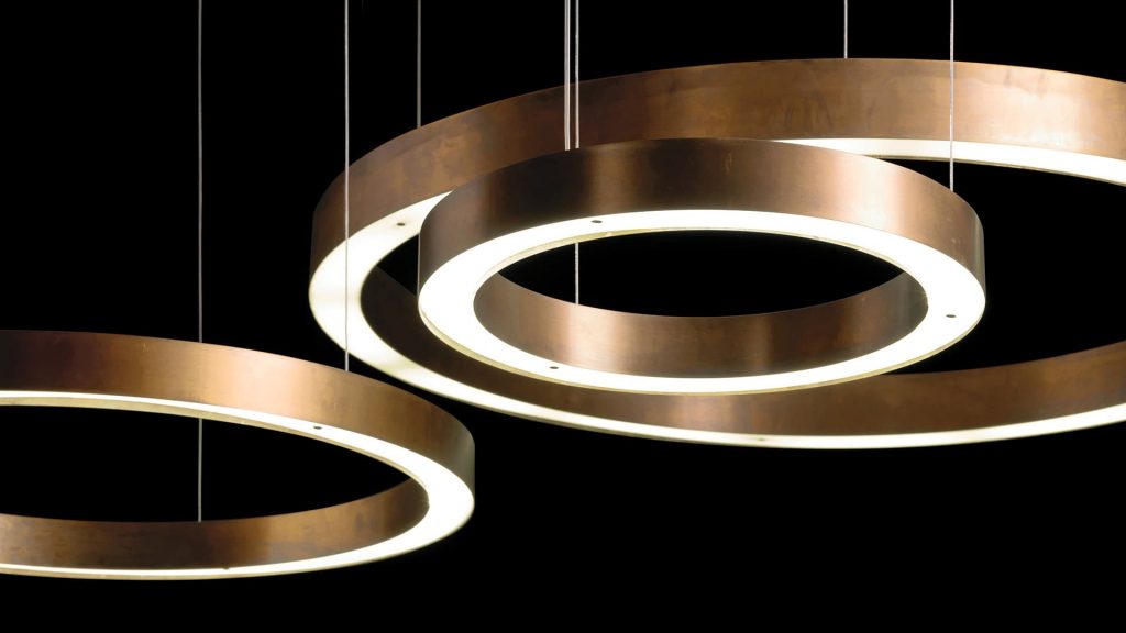 three ceiling lamps in the shape of thick rings in a gold tone on a black background