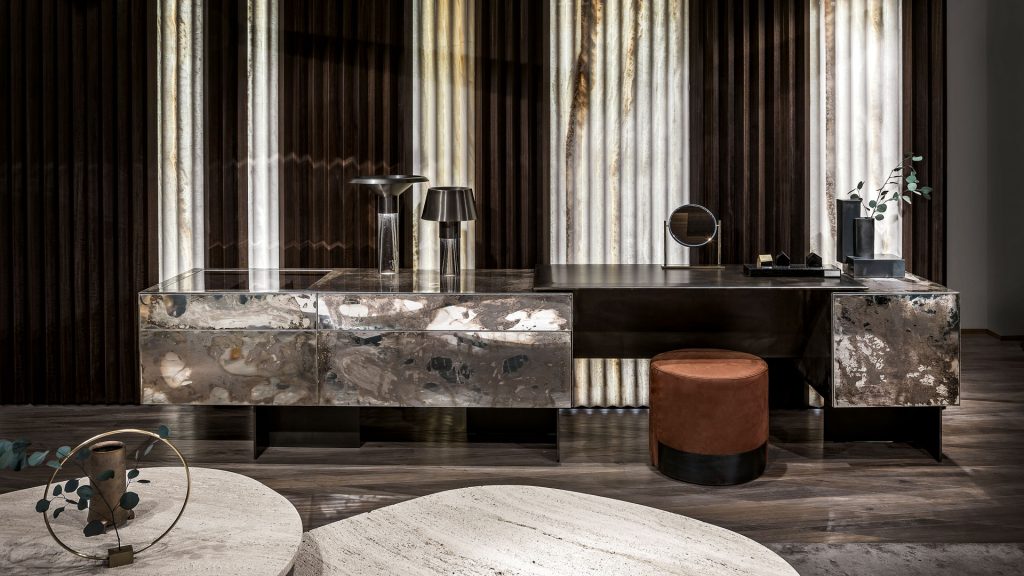 Noctis Vanity cabinet with three doors. Outside covered with burnished steel, three legs in black steel and a stool in a living room.