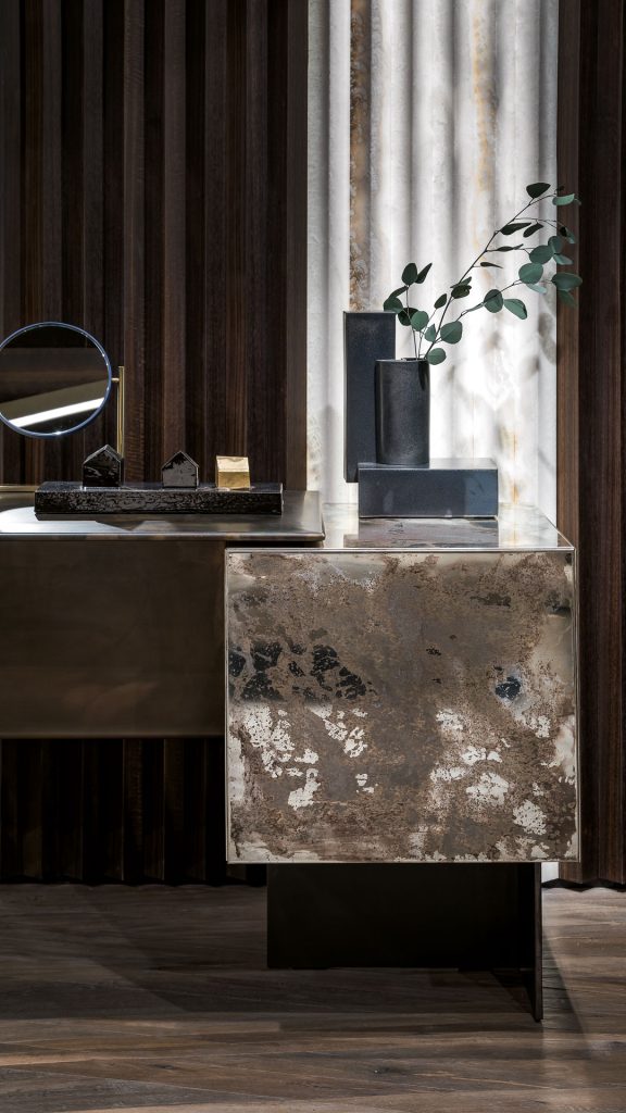 Closeup of Noctis Vanity cabinet with three doors. Outside covered with burnished steel, three legs in black steel in a living room.