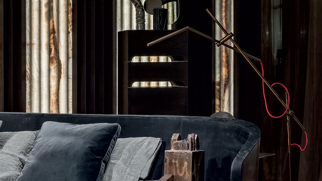 Pipe Light-L. L-shaped bronze lamp with a bulb at the end and red wiring in a bedroom.