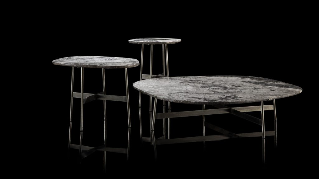 Three round Primitive Tables. Structure leg in metal rod finish burnished titanio. Top in white and black stone on a black background.