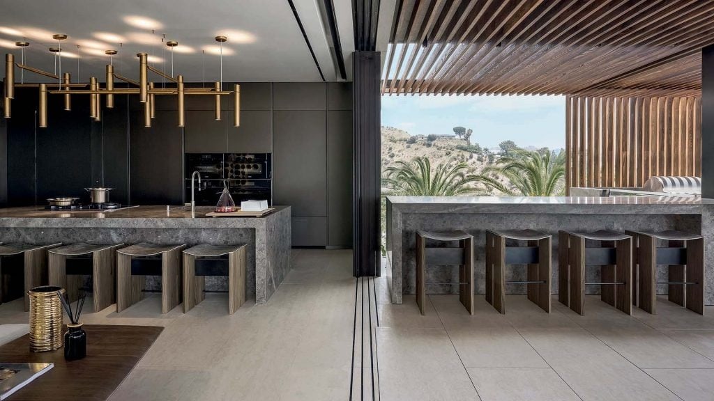 Eight Rio Stools, structure and two legs in natural wood with central crosspiece covered in brass; seat in gray leather in a kitchen.