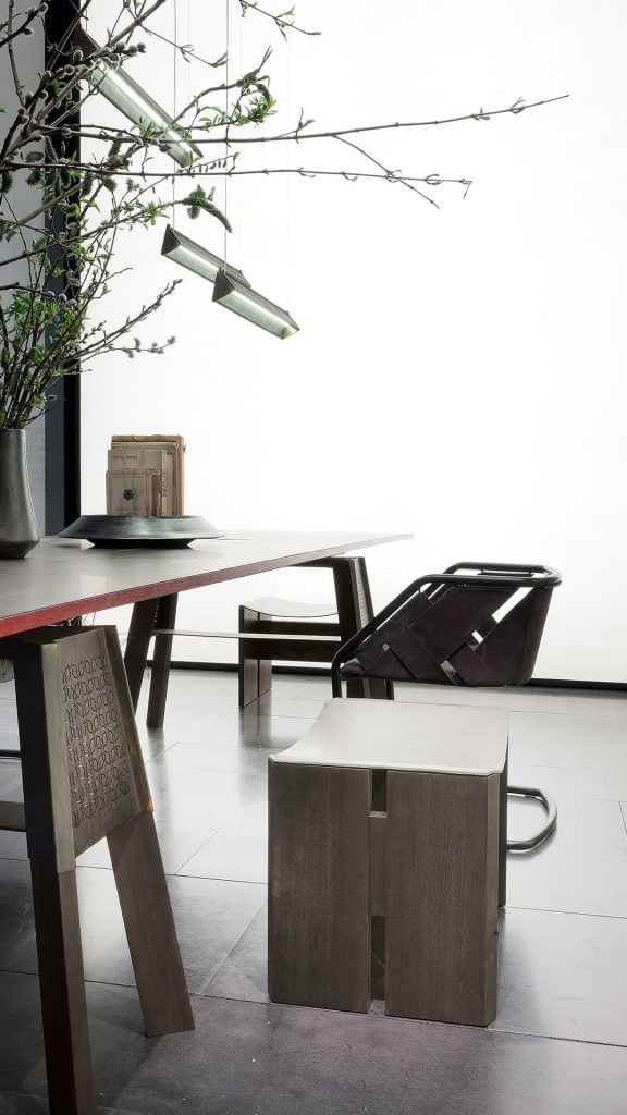 Rio Stool, structure and two legs in natural wood with central crosspiece covered in brass; seat in gray leather in a dining room.