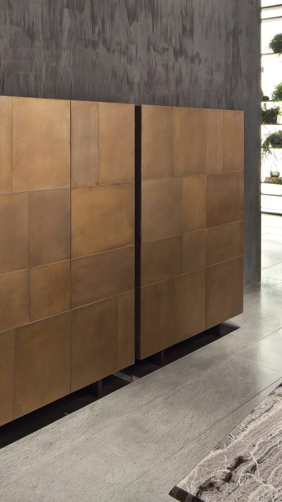 Two Slim Sides Vertical, finish and two legs in brass with a pattern of squares and rectangles on a gray room.