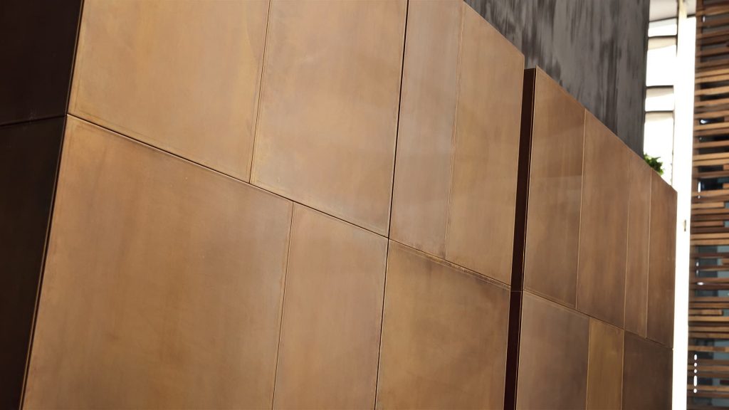 Two Slim Sides Vertical, finish and two legs in brass with a pattern of squares and rectangles on a gray room.
