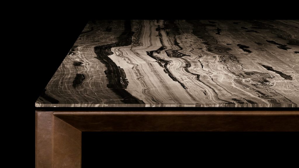 Closeup of Soprano dining table, structure and four legs in brown wood, top in white, grey, brown and black stone on a black background.
